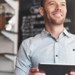 Image of a male business owner smiling, knowing his business social media is being taken care of, and holding a laptop.